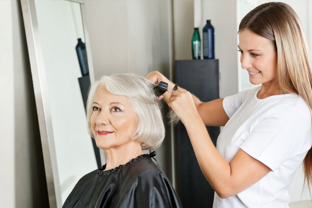 Senior woman getting her hair straightened by female hairstylist at salon
